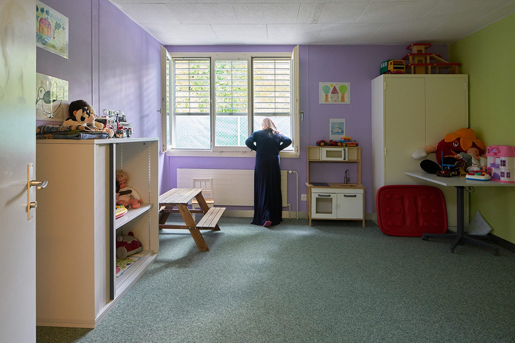 A woman wearing a headscarf stands looking out of the window in the federal asylum centre in Embrach.